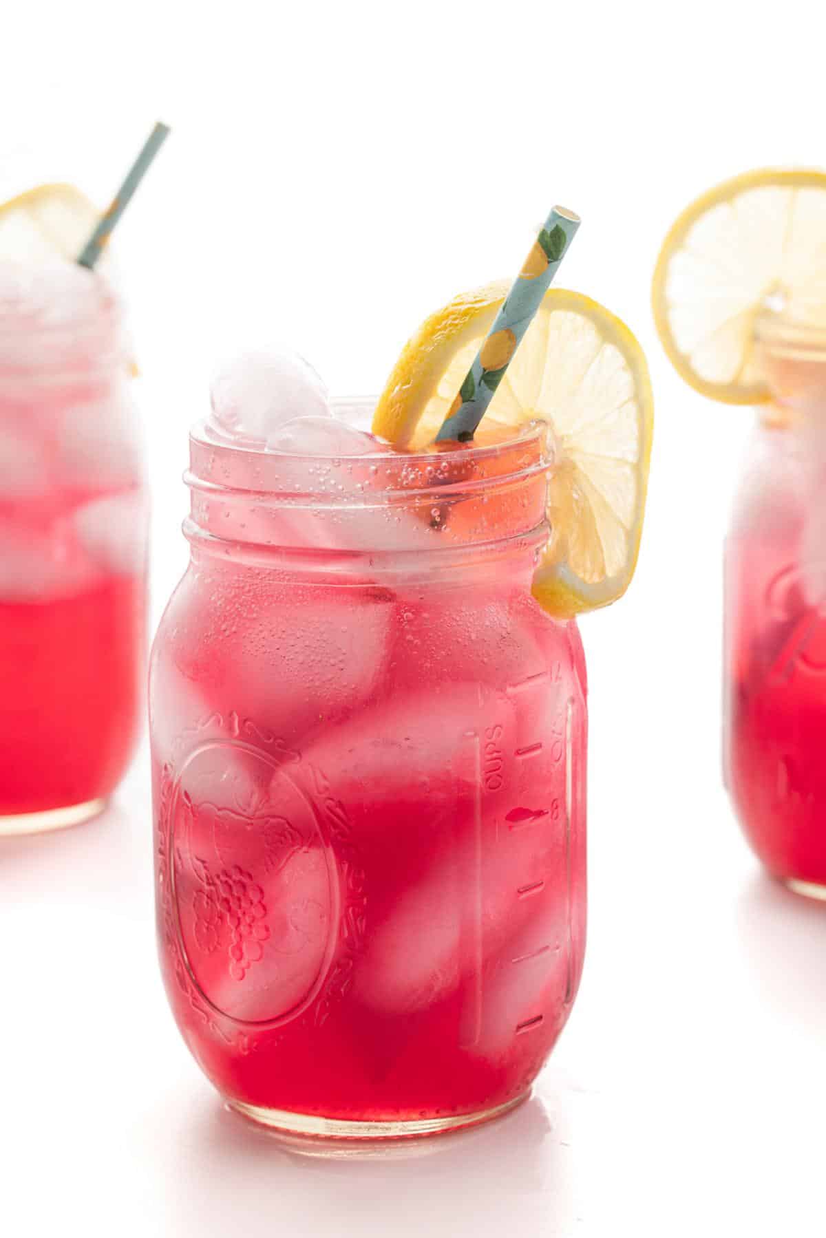 A blueberry vodka lemonade cocktail in a mason jar glass with a straw and garnished with a lemon slice.