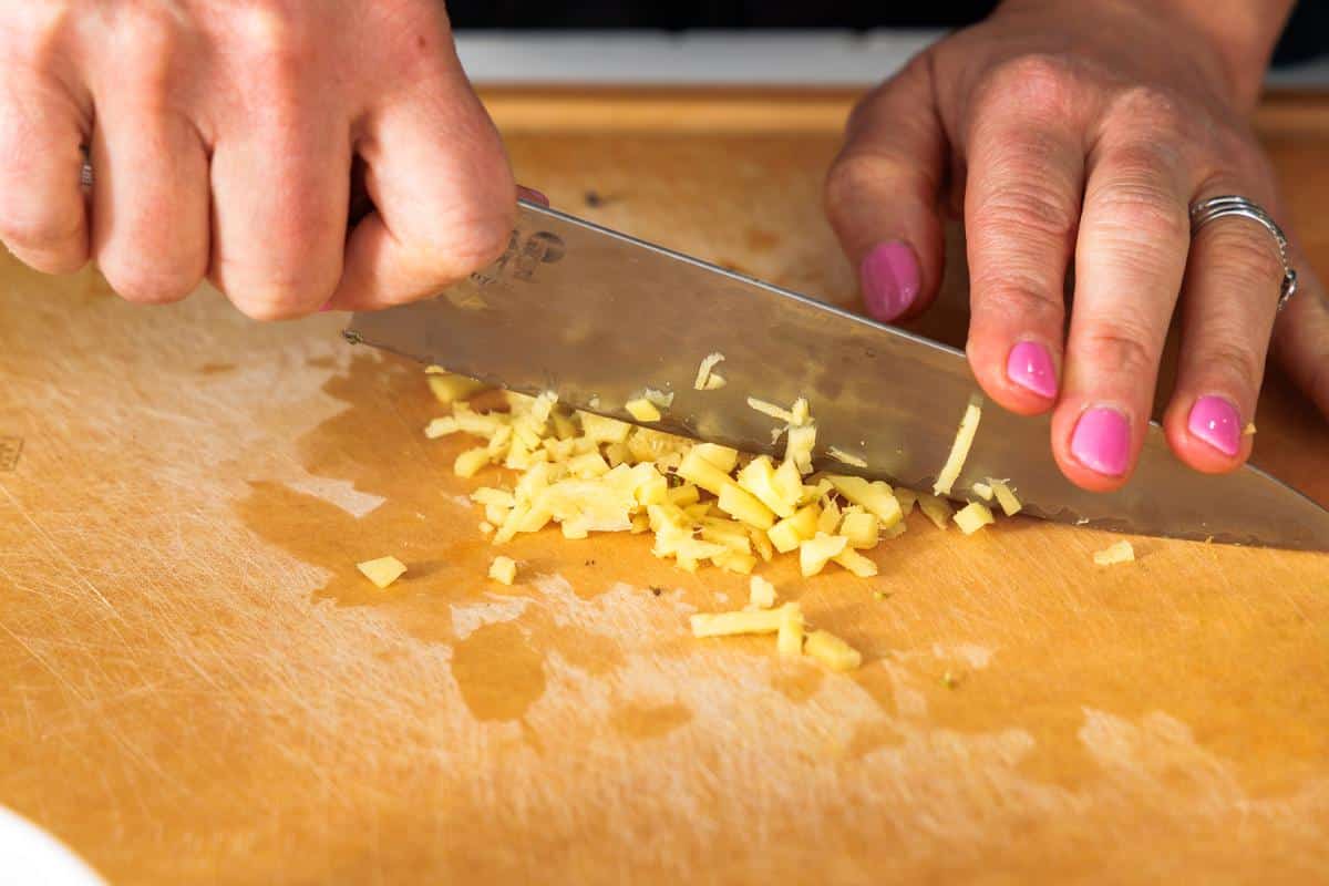 Mincing fresh ginger with a large knife.