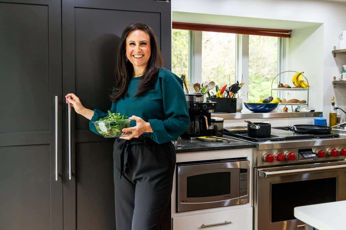Liz standing in front of her fridge in her kitchen with her microwave and wolf dual range in the background.