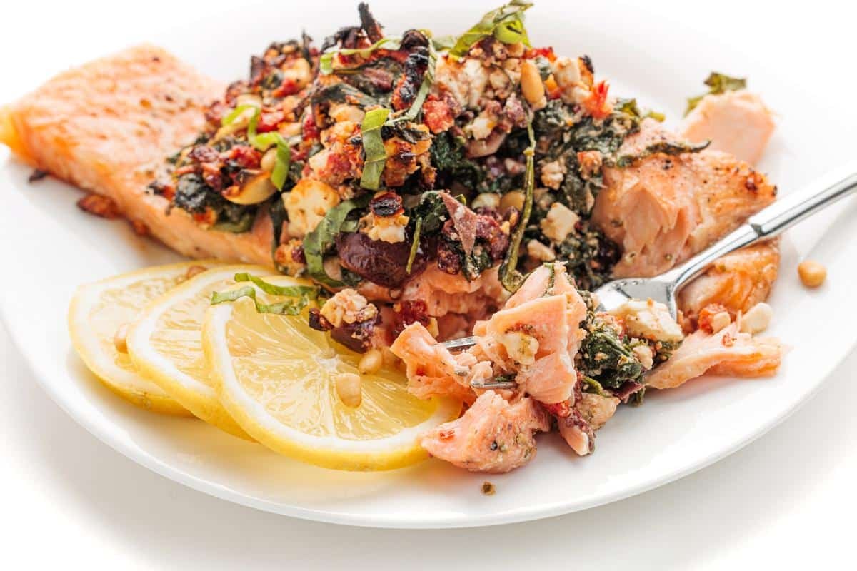 Mediterranean stuffed salmon on a plate with slices of lemon.