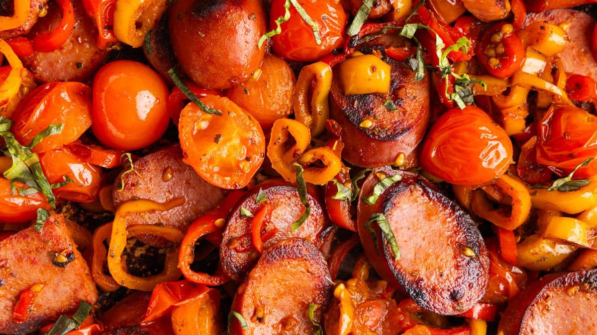 Smoked sausage skillet with tomatoes and peppers and garnished with basil.