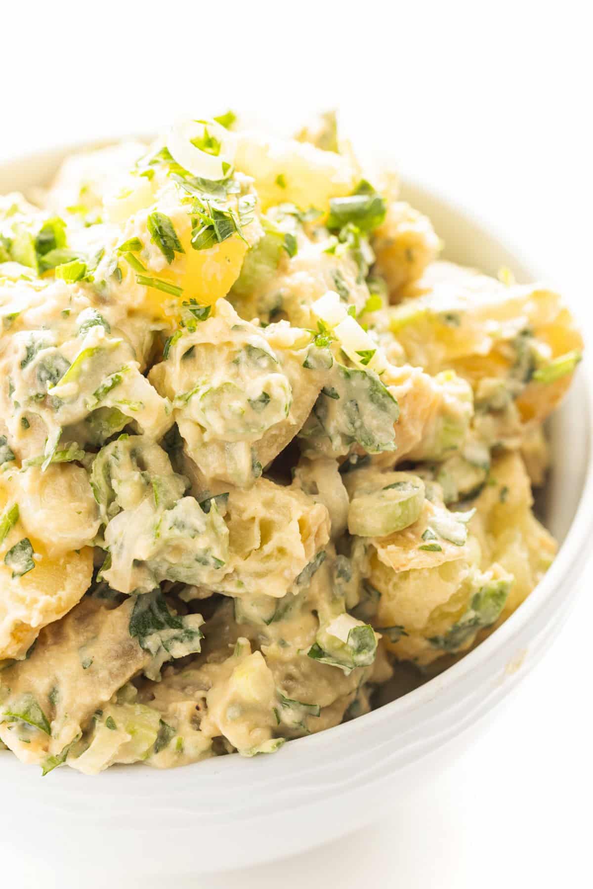 Vegan potato salad in a bowl topped with fresh mint and parsley.
