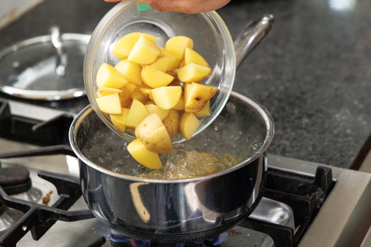 Adding cut potatoes to bowl of boiling water.