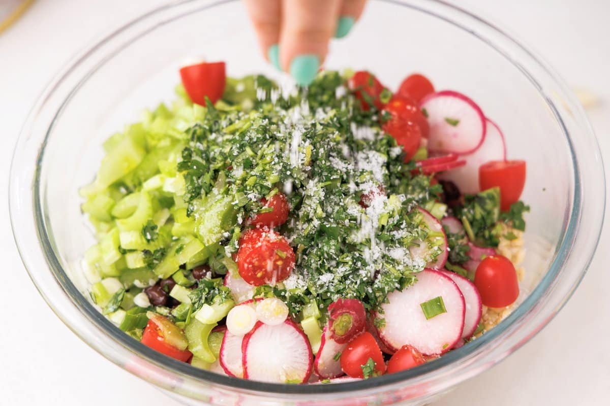 Adding fresh herbs and seasoning to salad.