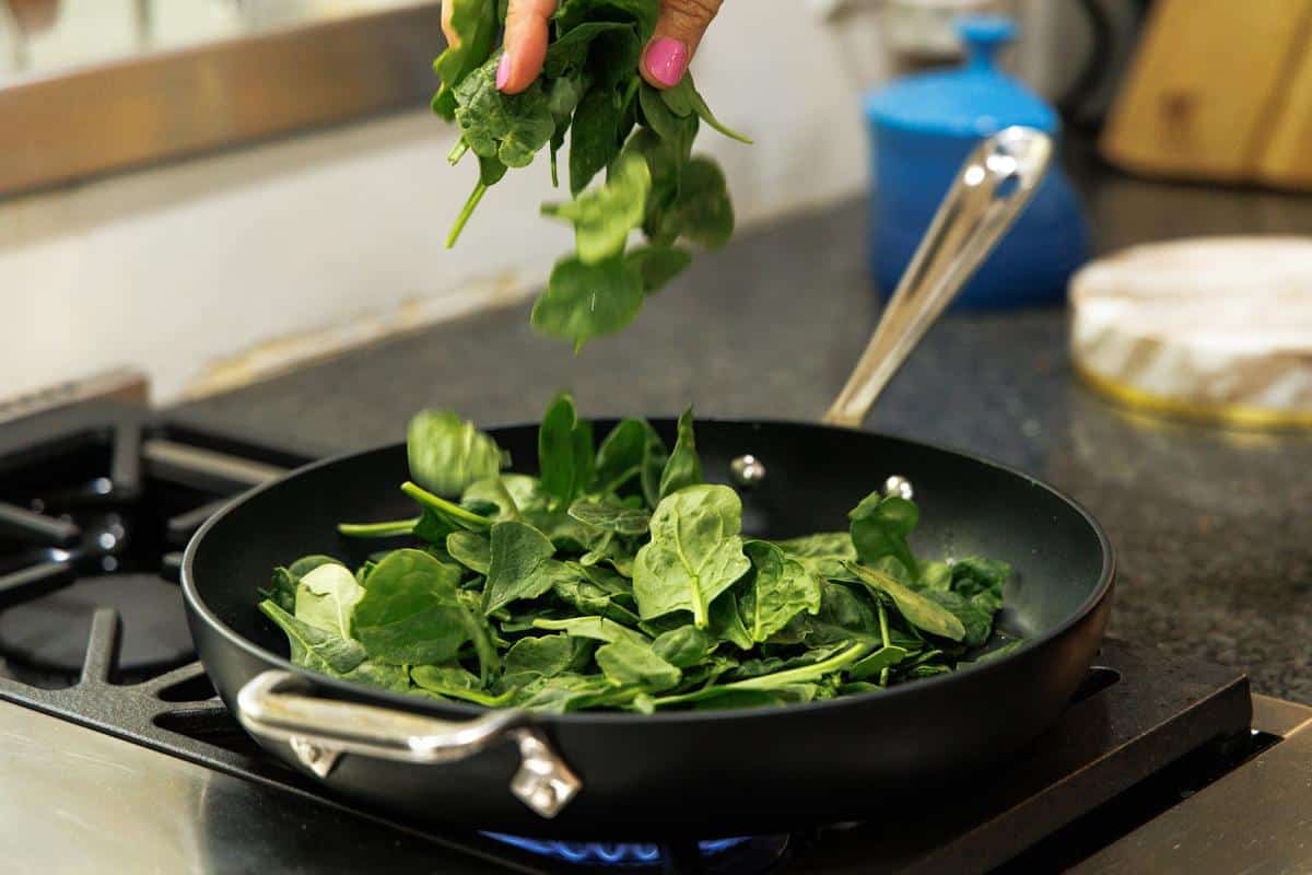 Adding spinach to skillet on the stove.
