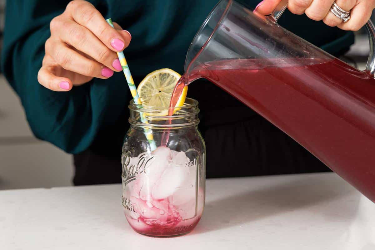 Pouring blueberry vodka lemonade into mason jar glass.