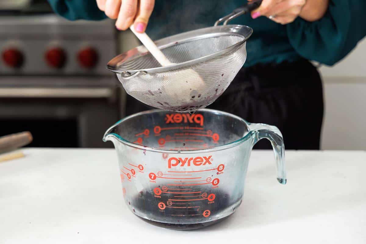 Straining blueberry simple syrup into a large glass bowl.