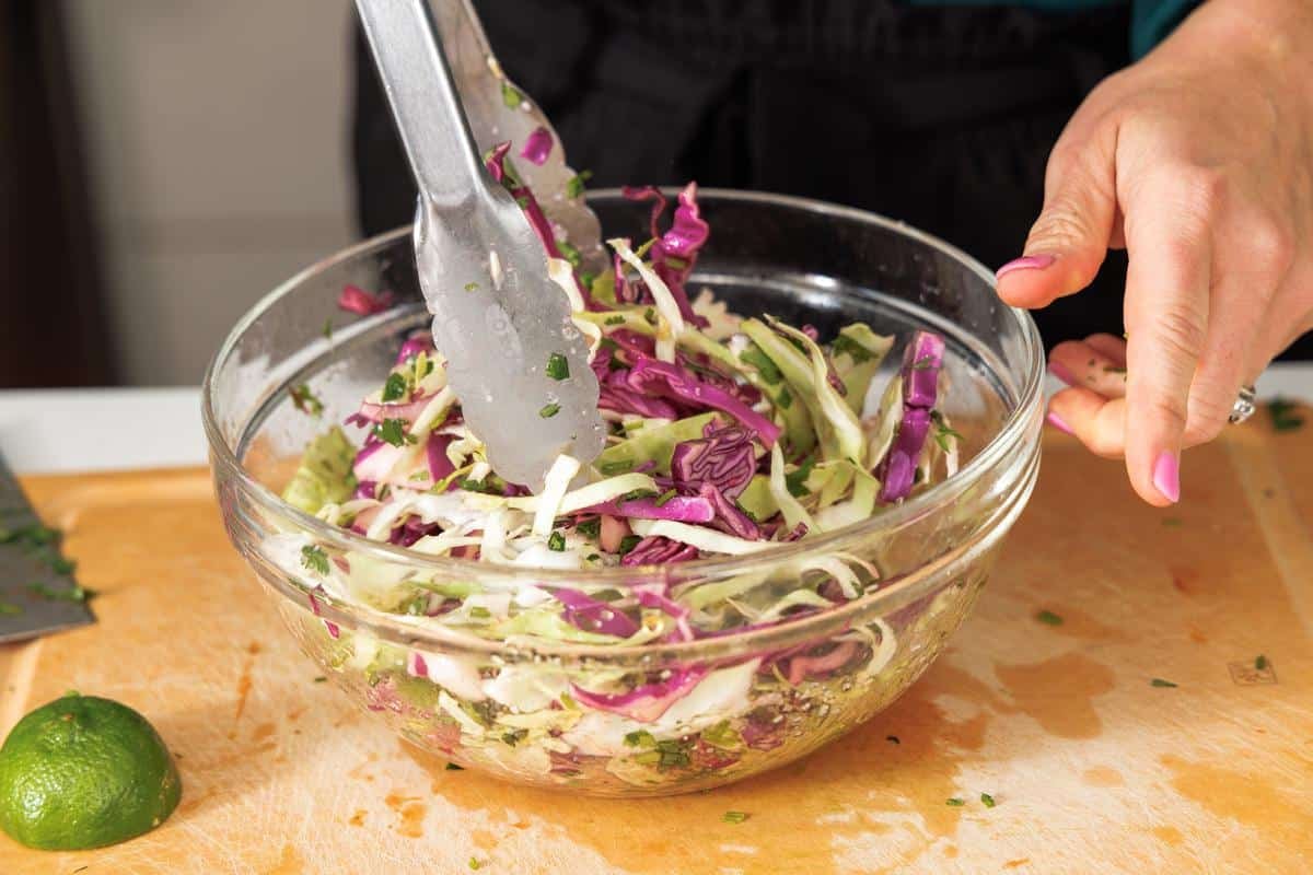 Tossing cabbage slaw in a large glass bowl.
