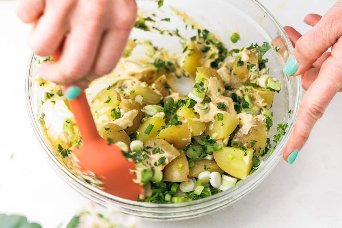 Stirring vegan potato salad in hummus dressing.