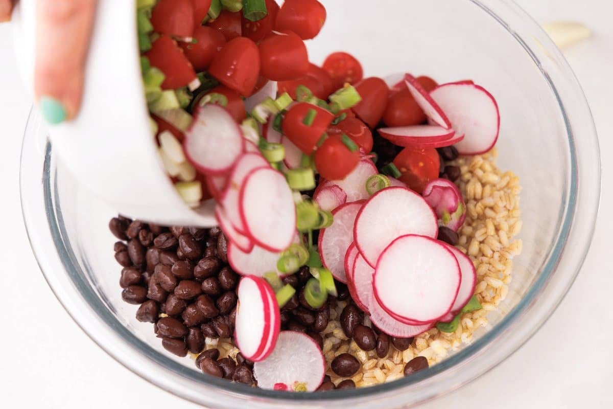 Adding fresh herbs and veggies to bowl with beans and barley.