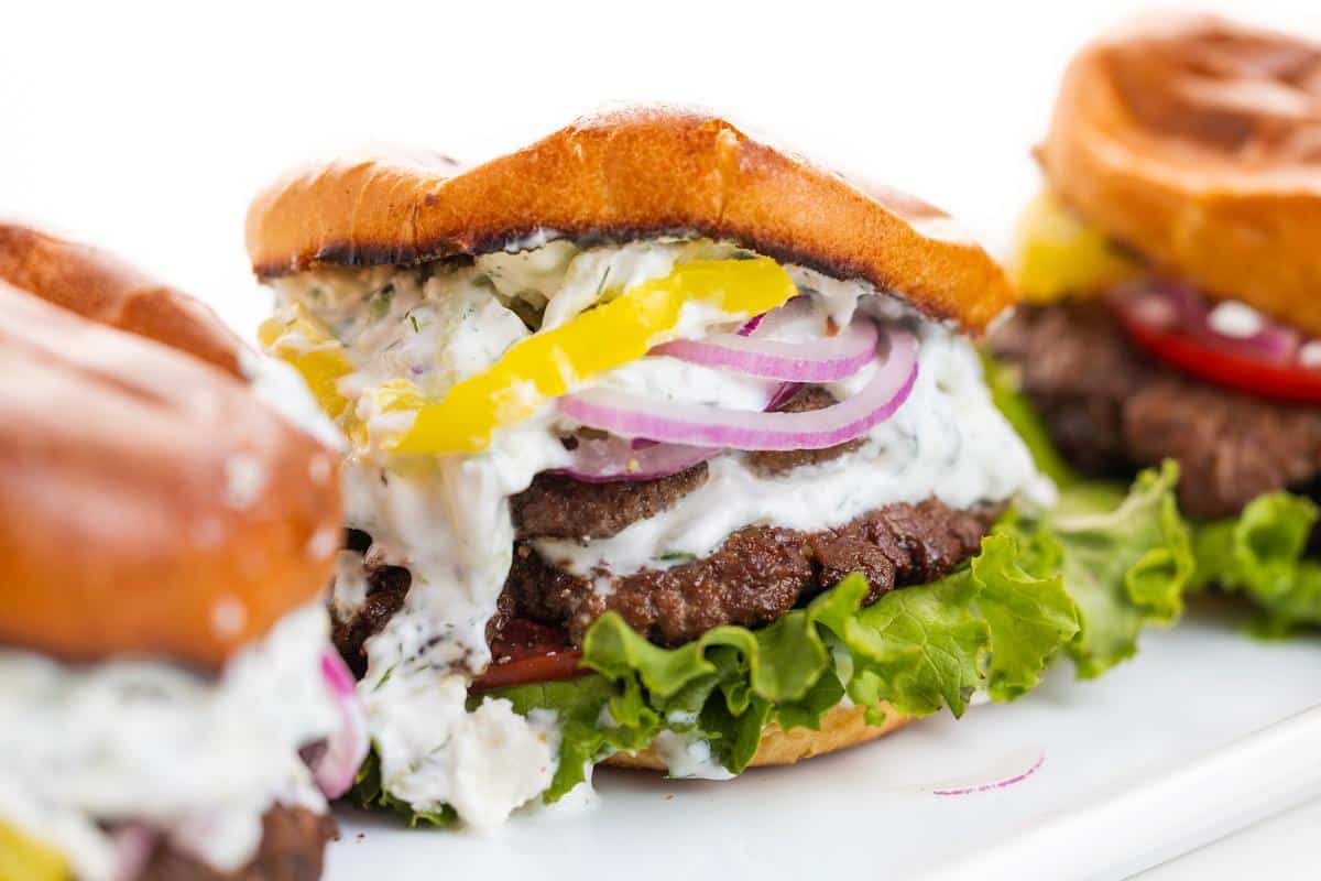 Three Greek smash burgers fully assembled on a platter.