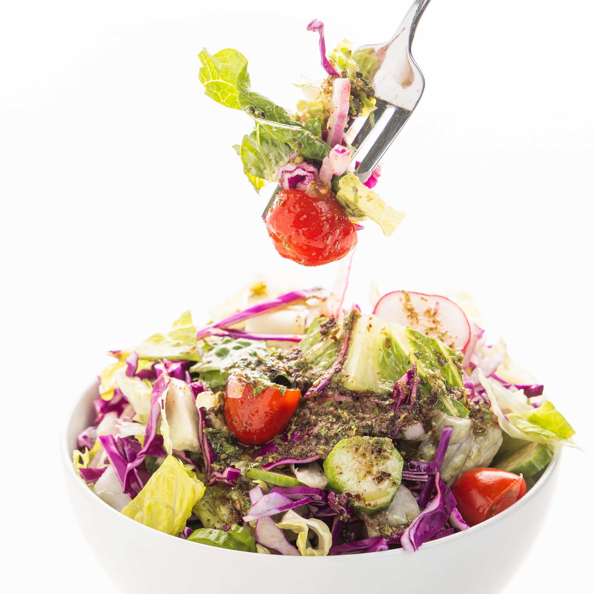A fork stabbing into a Mediterranean salad topped with Lebanese salad dressing with lemon and garlic.