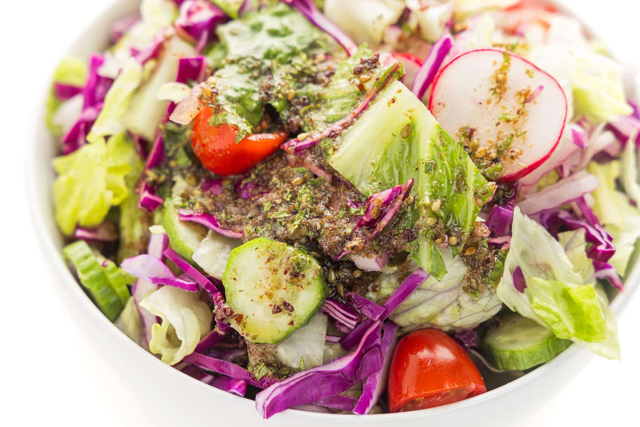 Close up on Lebanese salad dressing poured over the top of a Mediterranean green salad.