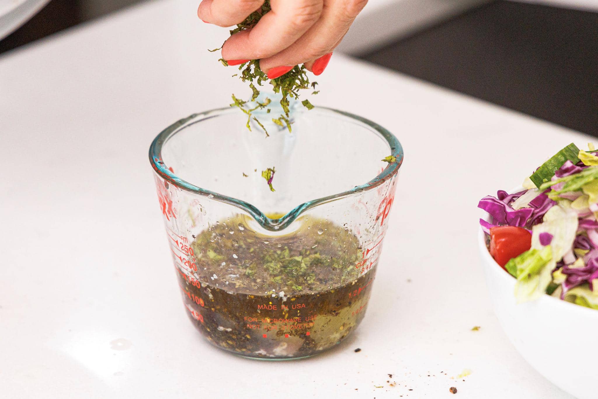 Sprinkling fresh mint to measuring cup with olive oil and lemon juice.
