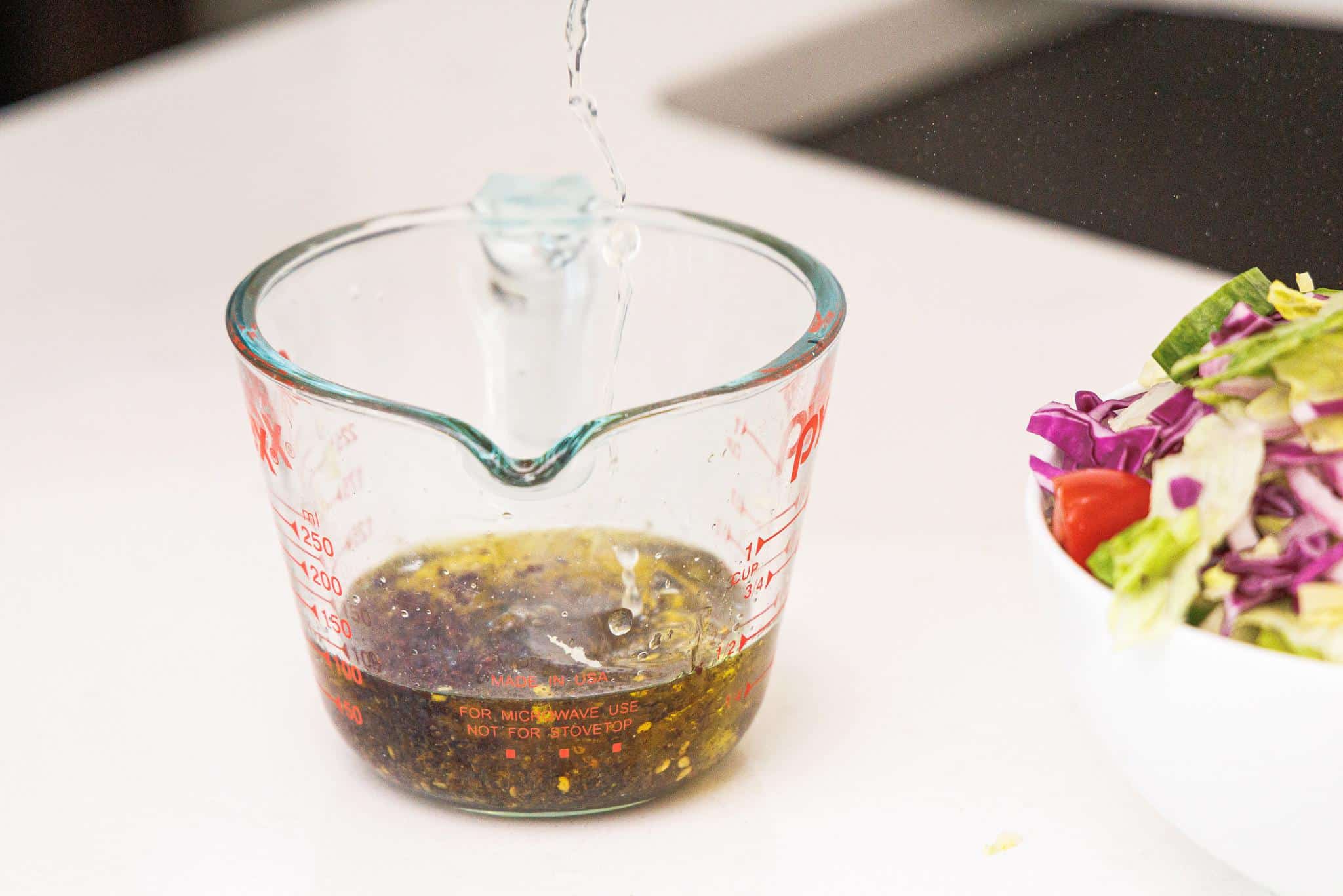 Adding lemon juice to a measuring cup with olive oil.