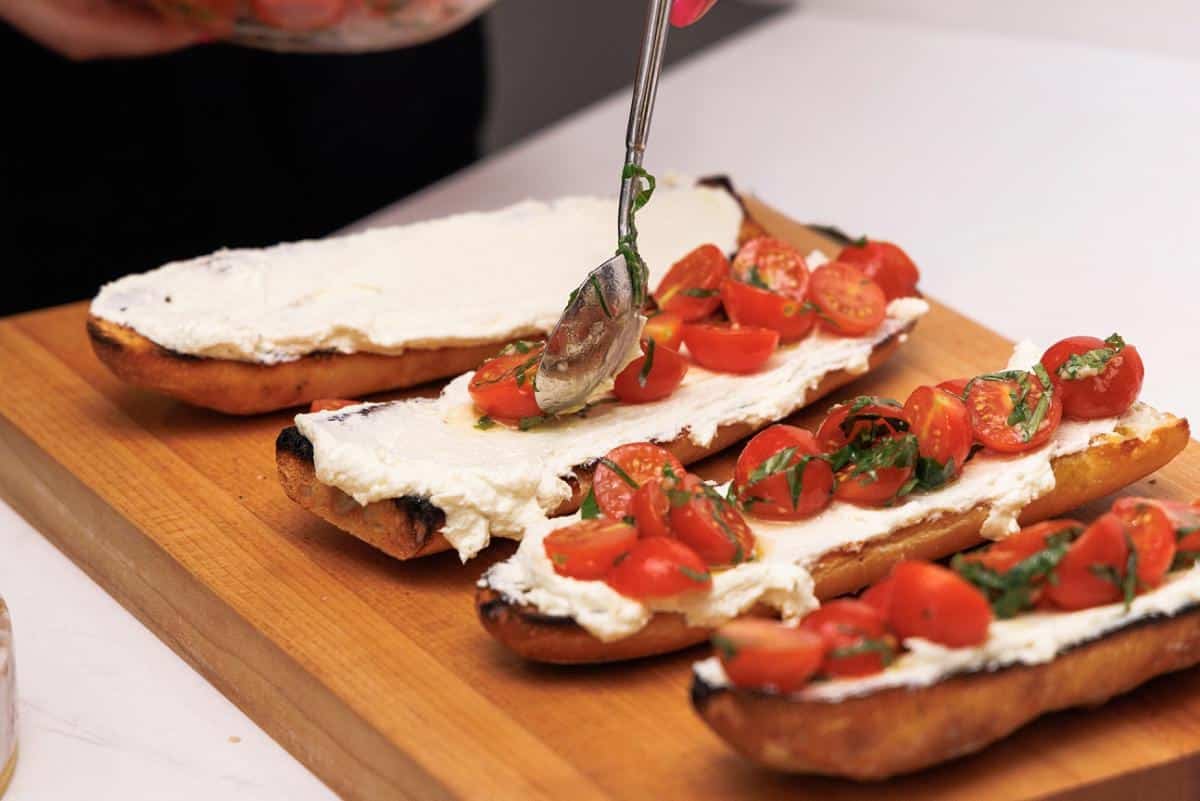 Scooping tomato topping onto slices of grilled Italian bread.