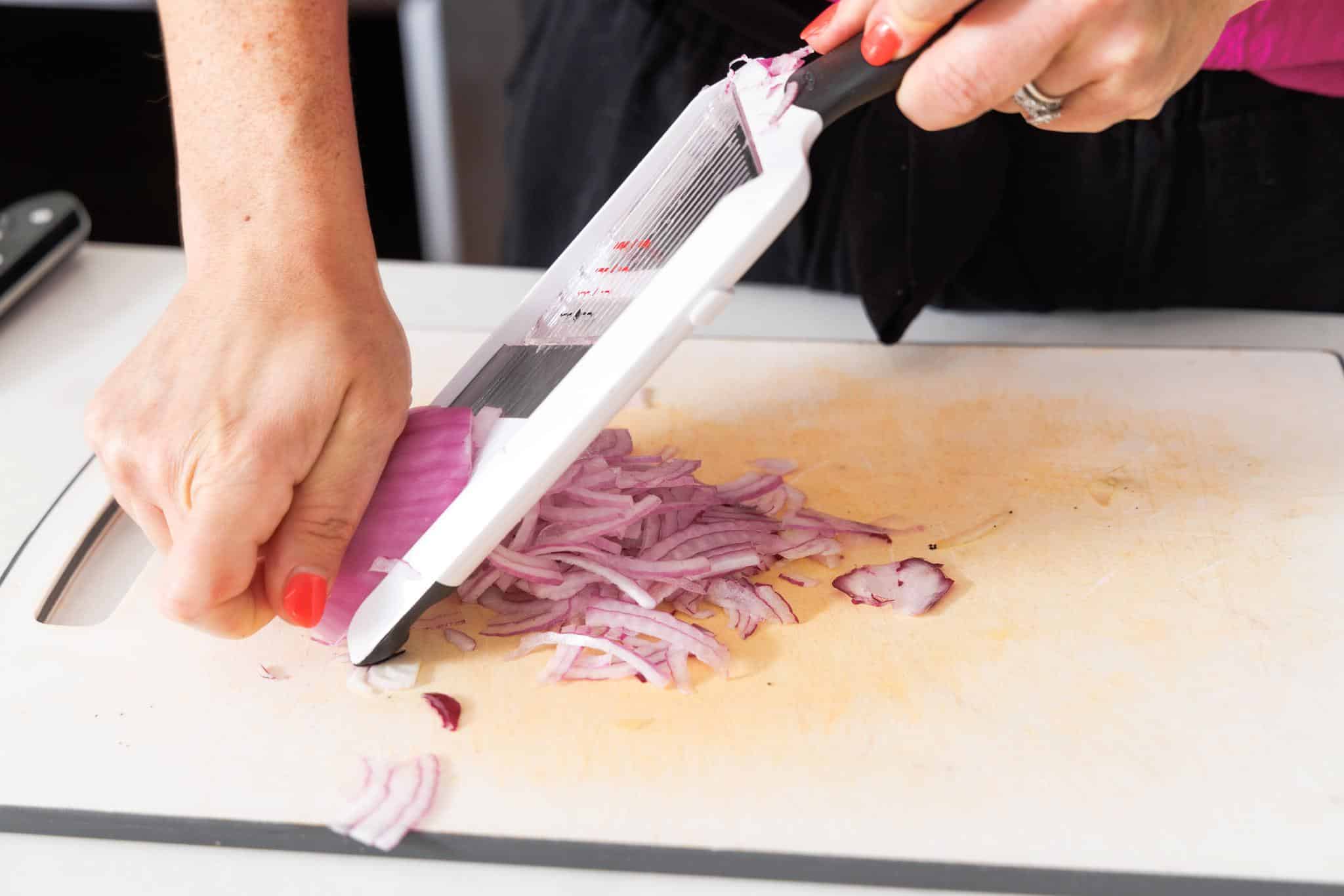 Using a mandolin to slice red onion into thin pieces.