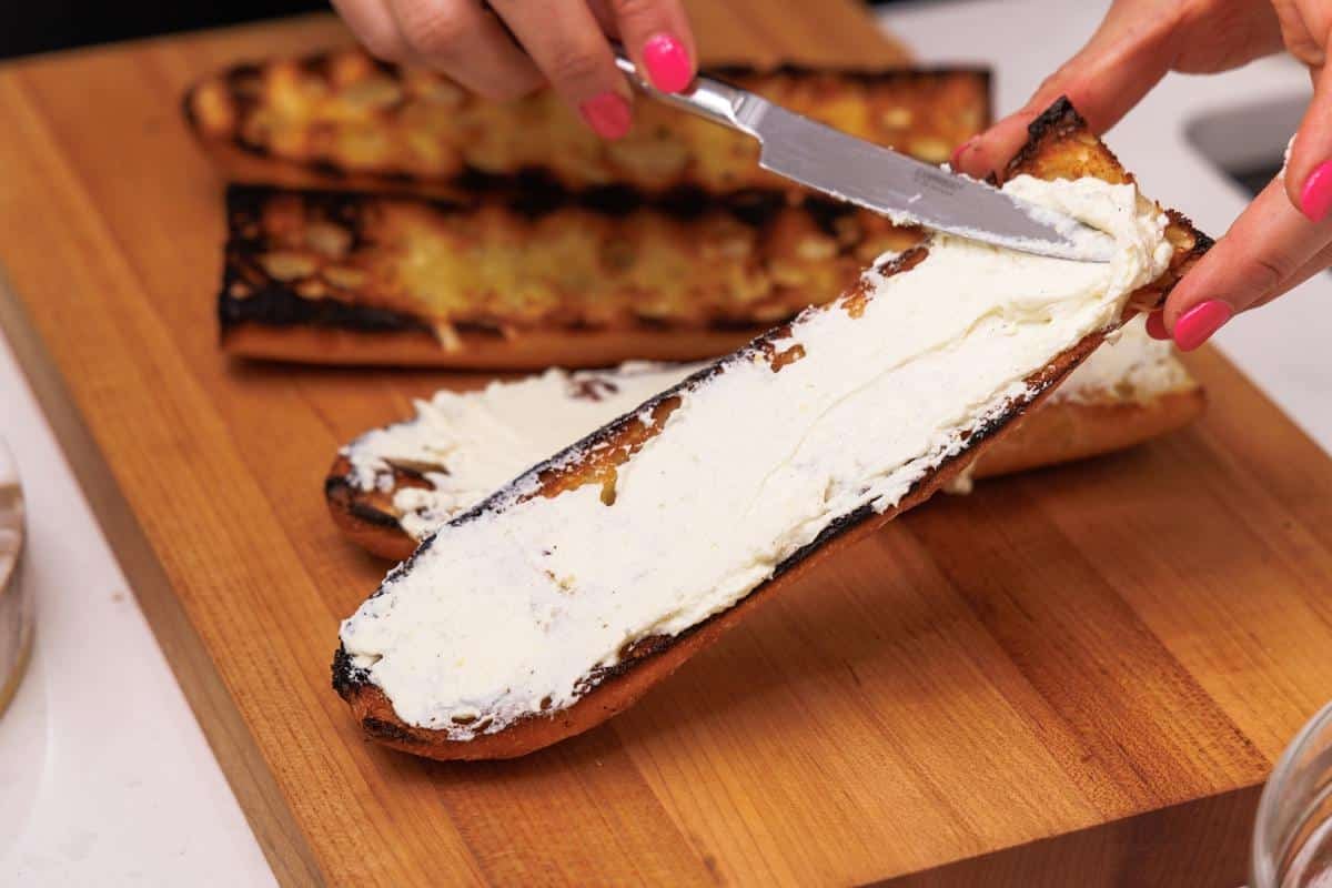 Spreading whipped feta onto grilled Italian bread slice.