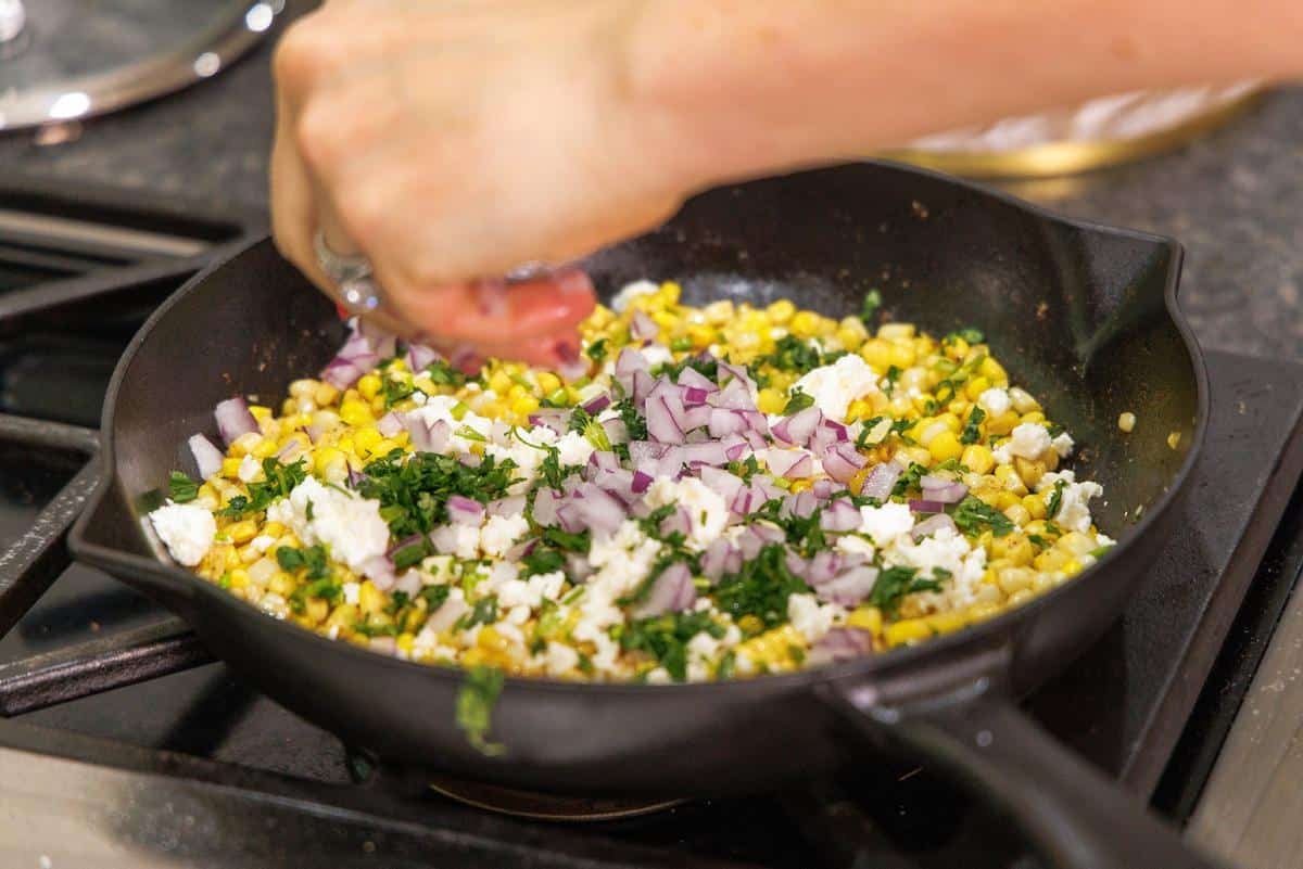 Adding cotija cheese to skillet with corn and onion.